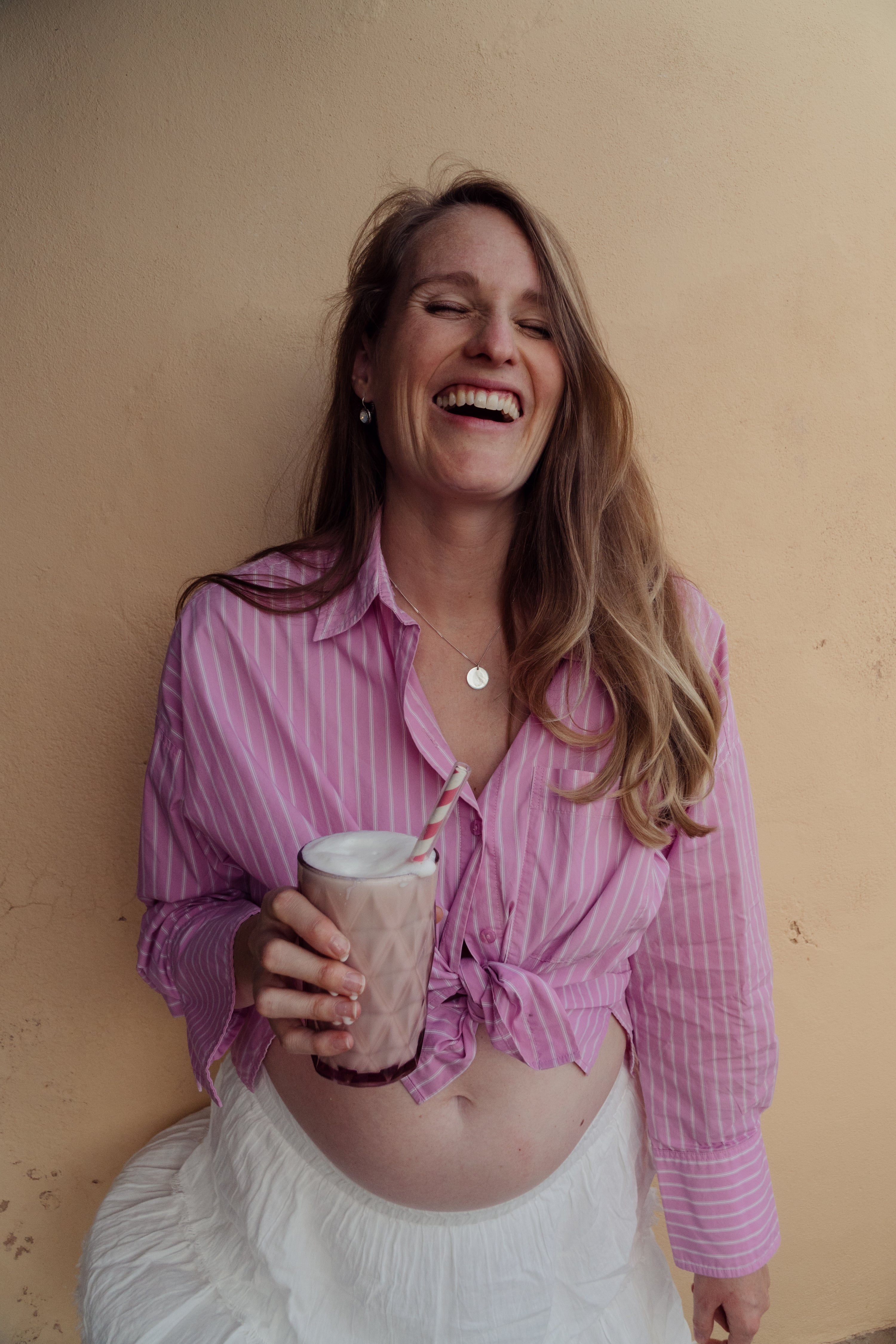 Woman in a pink shirt holding a the MomShake in front og a beige wall on Ibiza